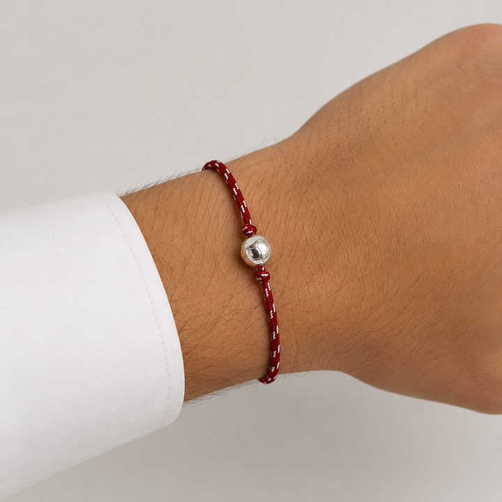Bracelet football rouge et blanc avec ballon argenté porté au poignet d’un homme
